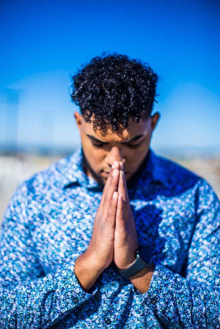 standing man in blue dress shirt praying